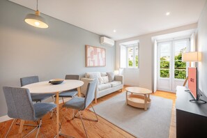 Ein modernes Wohnzimmer mit einem runden Esstisch, grauen Polsterstühlen, einem Sofa und einem Couchtisch.