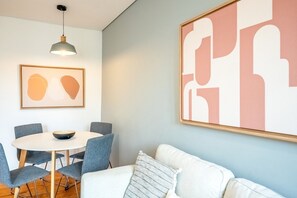 Ein modernes Wohnzimmer mit einem runden Esstisch, blauen Stühlen, einem weißen Sofa und abstrakter Kunst an den Wänden.