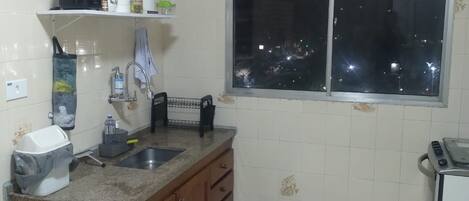 Una cocina con encimera de granito, un lavamanos, una ventana y un refrigerador pequeño.