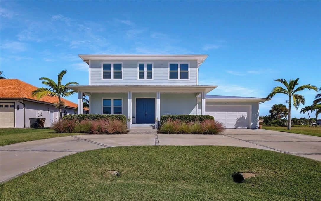 A two-story residential house with a front garage, a well-maintained lawn, and palm trees in the background.