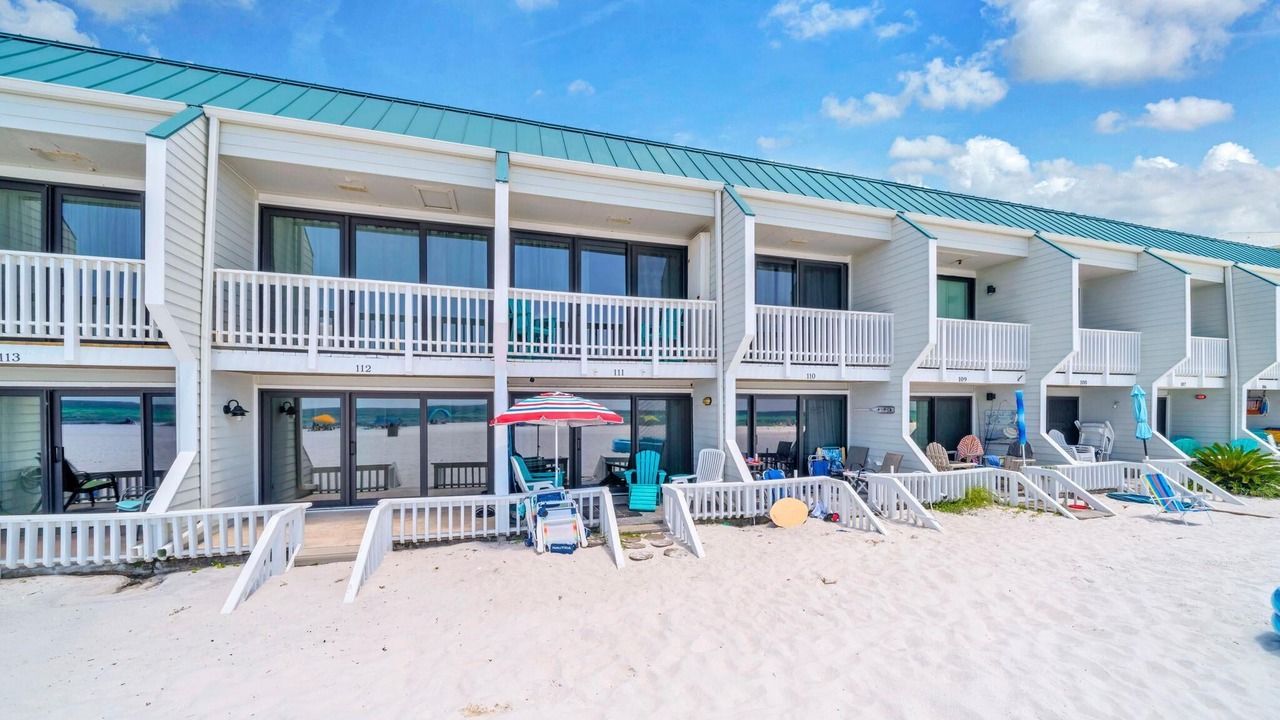 A beachfront motel with multiple balconies, outdoor seating, and a sandy beach area.