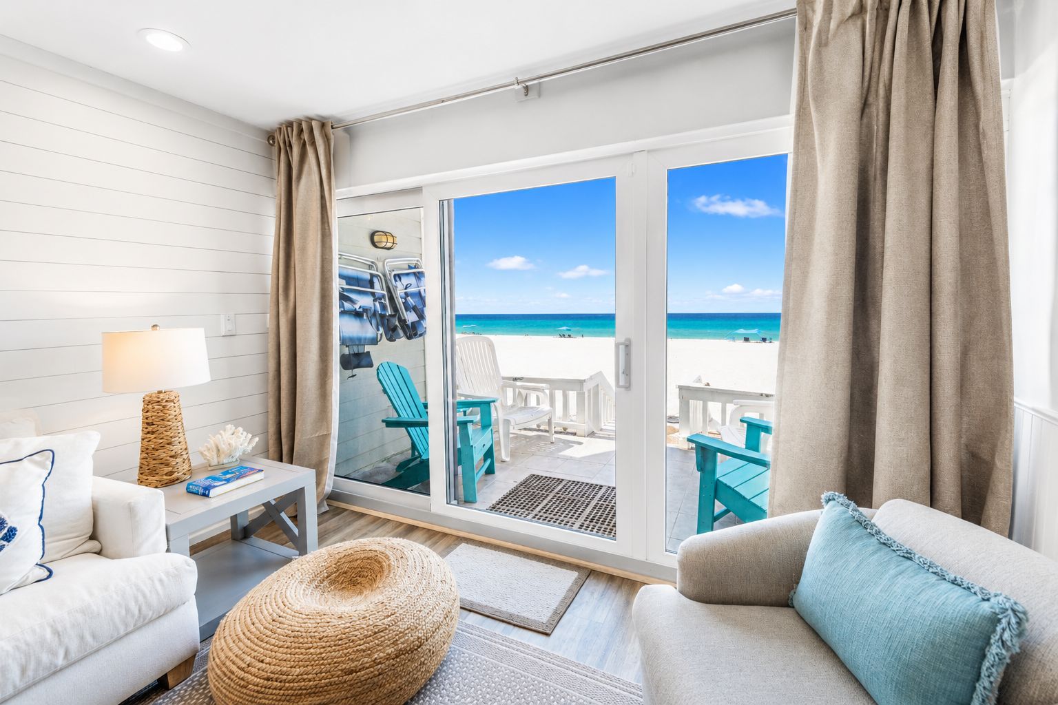 Une pièce avec vue sur la plage, un canapé blanc, un fauteuil bleu et une petite table avec une lampe.