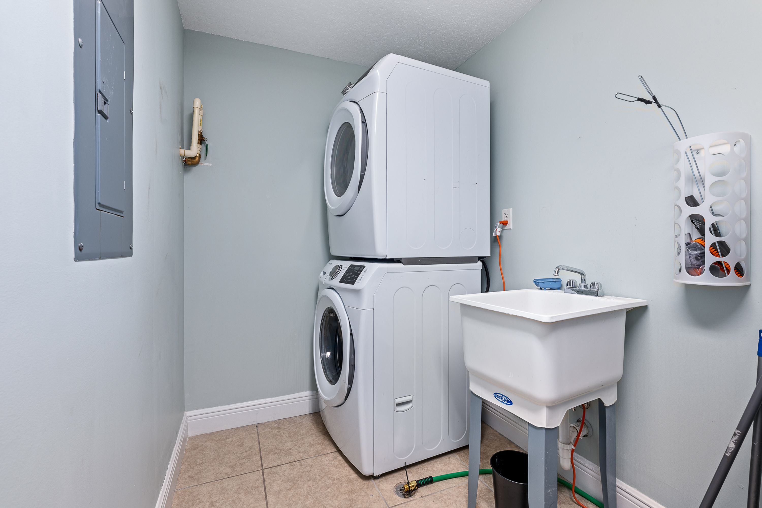 A laundry room with a stacked washer and dryer, a sink, and a wall-mounted paper towel dispenser.