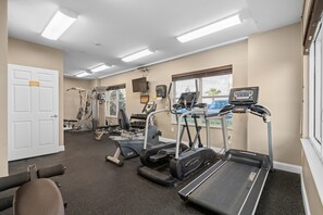 Ein Fitnessstudio mit Laufbändern, Kraftgeräten und einem Bildschirm.