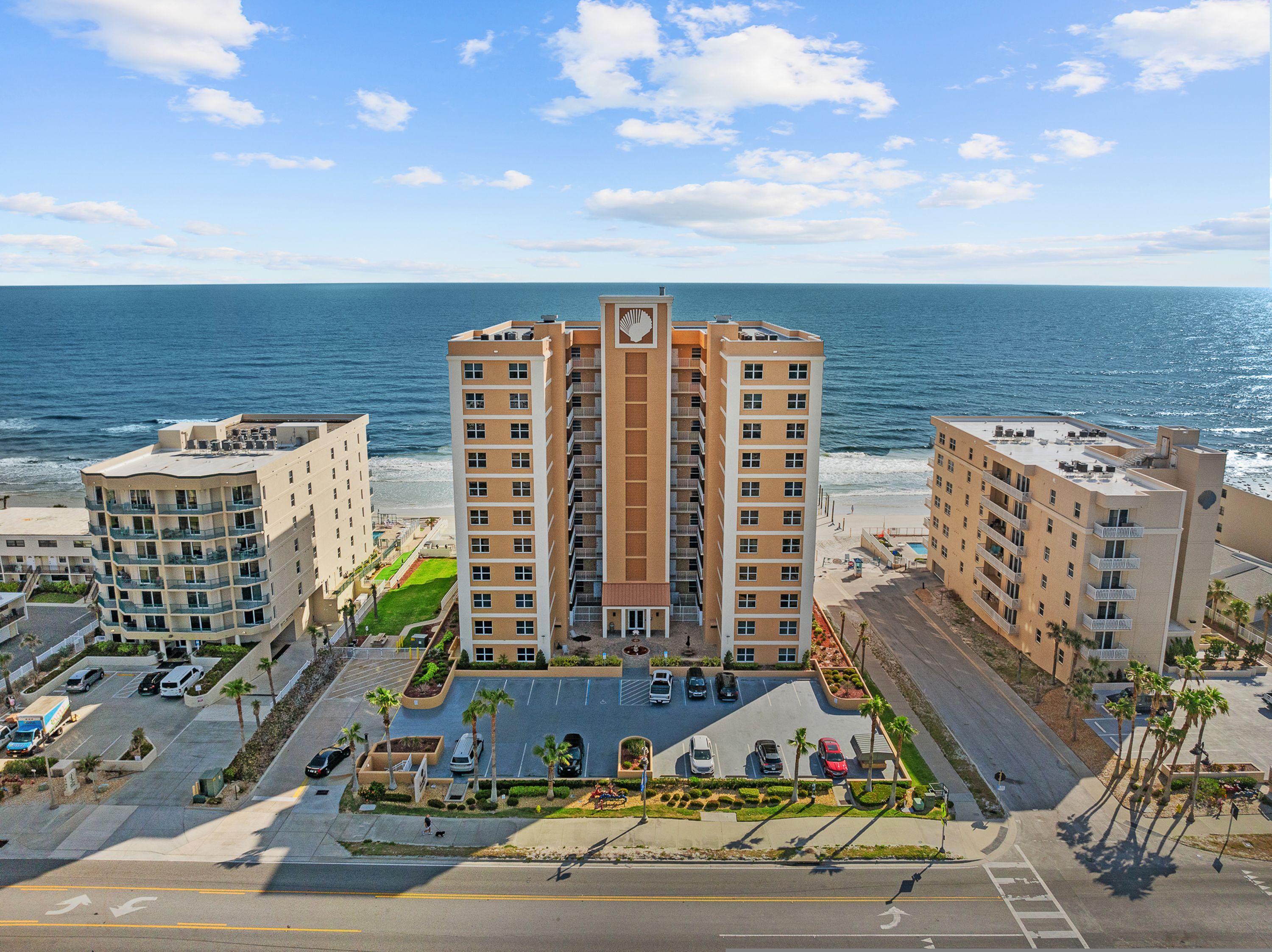 A beachfront hotel with multiple buildings, a parking lot, and a view of the ocean.