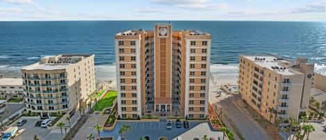 A beachfront hotel with multiple buildings, a parking lot, and a view of the ocean.