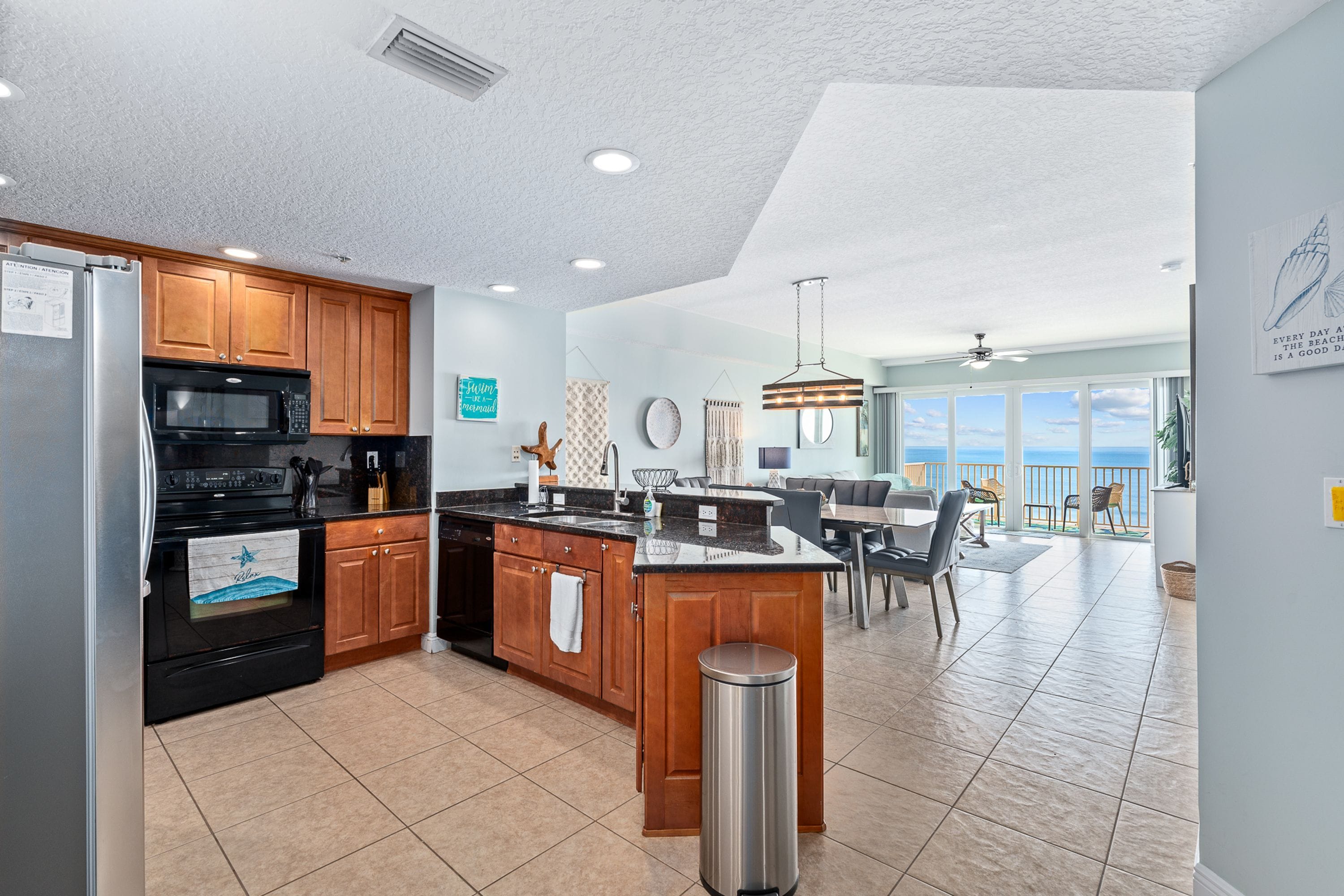 A spacious kitchen with wooden cabinets, a stainless steel refrigerator, and a large island with a sink.
