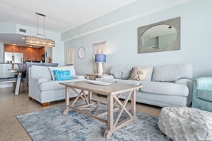 A modern living room with a grey sofa, a wooden coffee table, and a blue rug. - Oceanfront 3BR 3BA Condo With Large Balcony (Daytona Beach Shores)