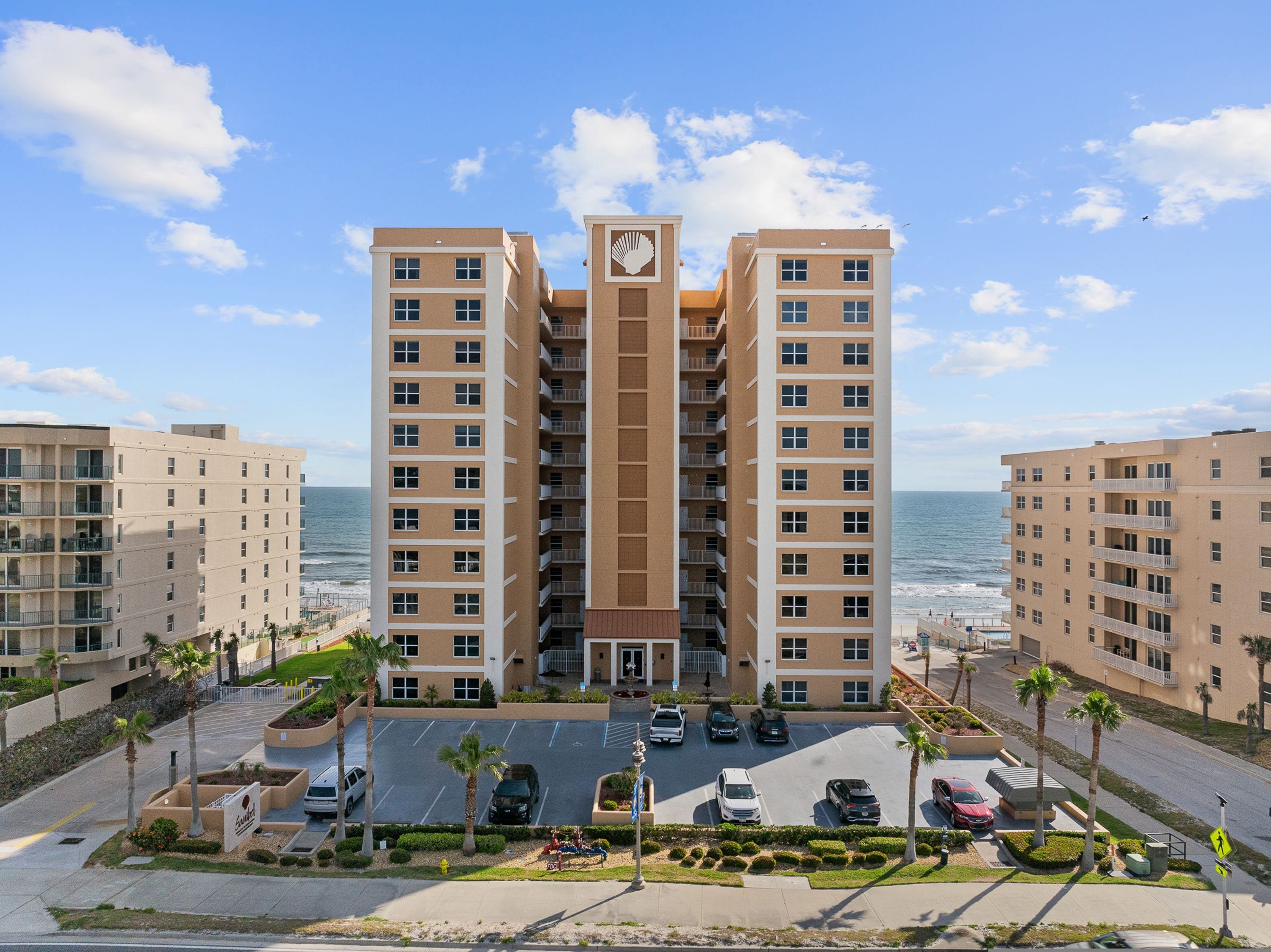 Un hôtel à plusieurs étages, doté d’une entrée principale, d’un parking et offrant une vue sur l’océan.