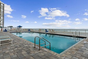 A swimming pool with a view of the ocean, a beach, and a tall building in the background. - Oceanfront 3BR 3BA Condo With Large Balcony (Daytona Beach Shores)