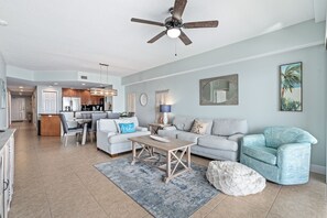 A spacious living area with a ceiling fan, a dining table with chairs, a sofa, and a blue armchair. - Oceanfront 3BR 3BA Condo With Large Balcony (Daytona Beach Shores)