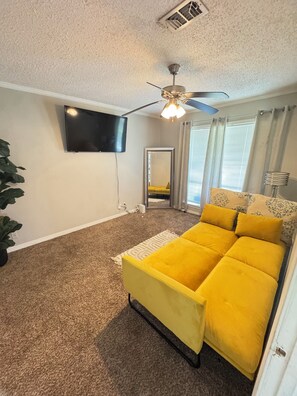 A bedroom with a bed, a ceiling fan, a TV, and a window with curtains. - The Luxe Haven - 3BR • Huge Gated Yard • Private Patio (Mobile)
