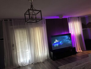Una sala de estar con televisor de pantalla plana, cortinas y una lámpara colgante.
