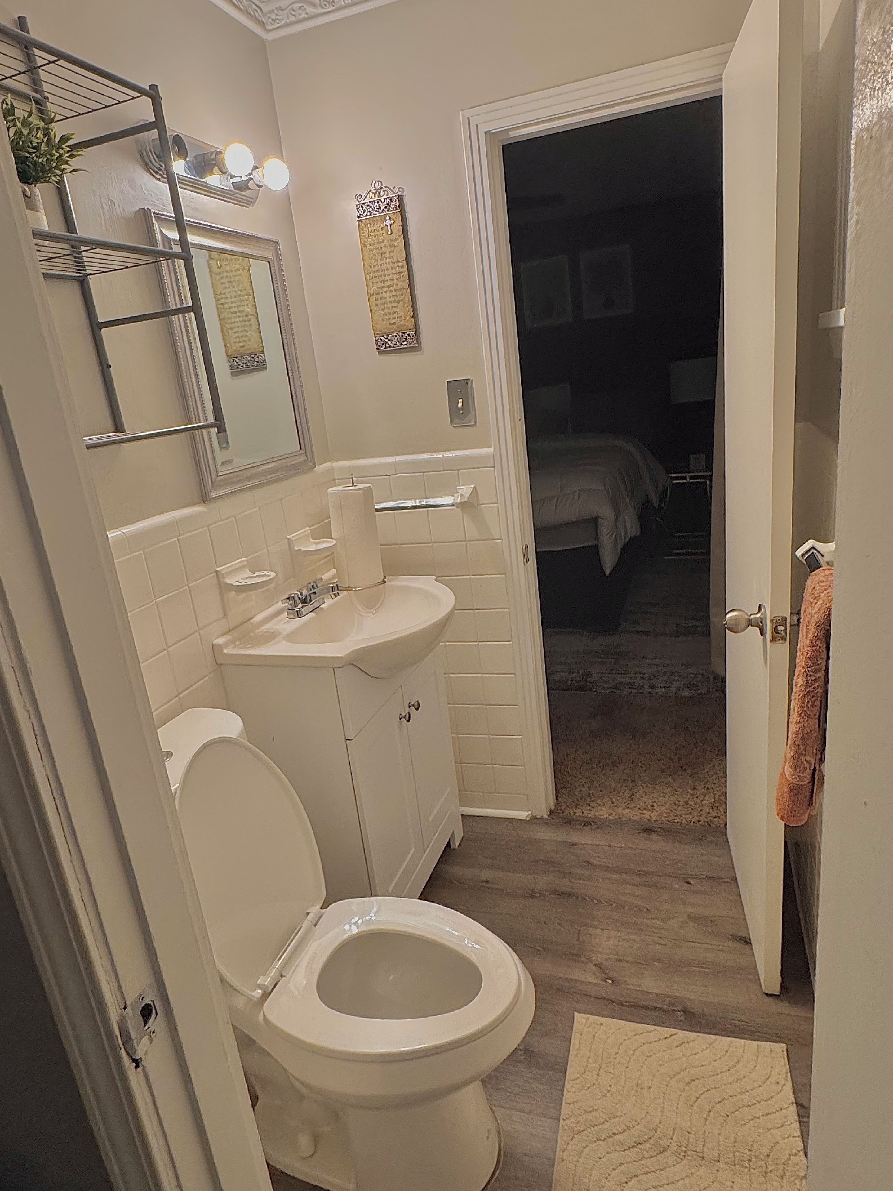 A bathroom with a toilet, sink, and mirror. There is a towel rack and a door leading to a bedroom.