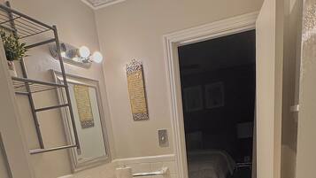 A bathroom with a toilet, sink, and mirror. There is a towel rack and a door leading to a bedroom.