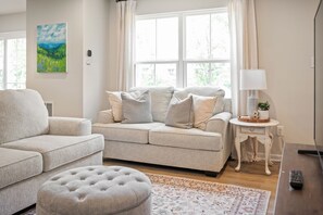 A living room with a sofa, ottoman, and a side table with a lamp. - Modern Family Retreat Near Liberty University (Lynchburg)