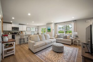 Un salon moderne comprenant un canap é, un pouf et un coin cuisine avec un four à micro-ondes et des placards.