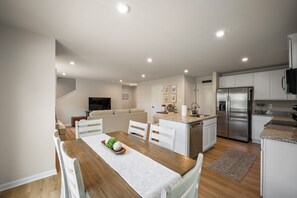A modern kitchen with a built-in refrigerator, a dining area with a wooden table and chairs, and a living area with a sofa and a flat-screen TV. - Modern Family Retreat Near Liberty University (Lynchburg)