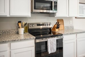 Une cuisine moderne dotée d’une cuisinière en acier inoxydable, d’un four à micro-ondes placé au-dessus et d’un comptoir en granit.