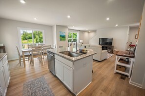 A modern kitchen with a central island, dining area with chairs, a sofa, and a TV in a living area. - Modern Family Retreat Near Liberty University (Lynchburg)
