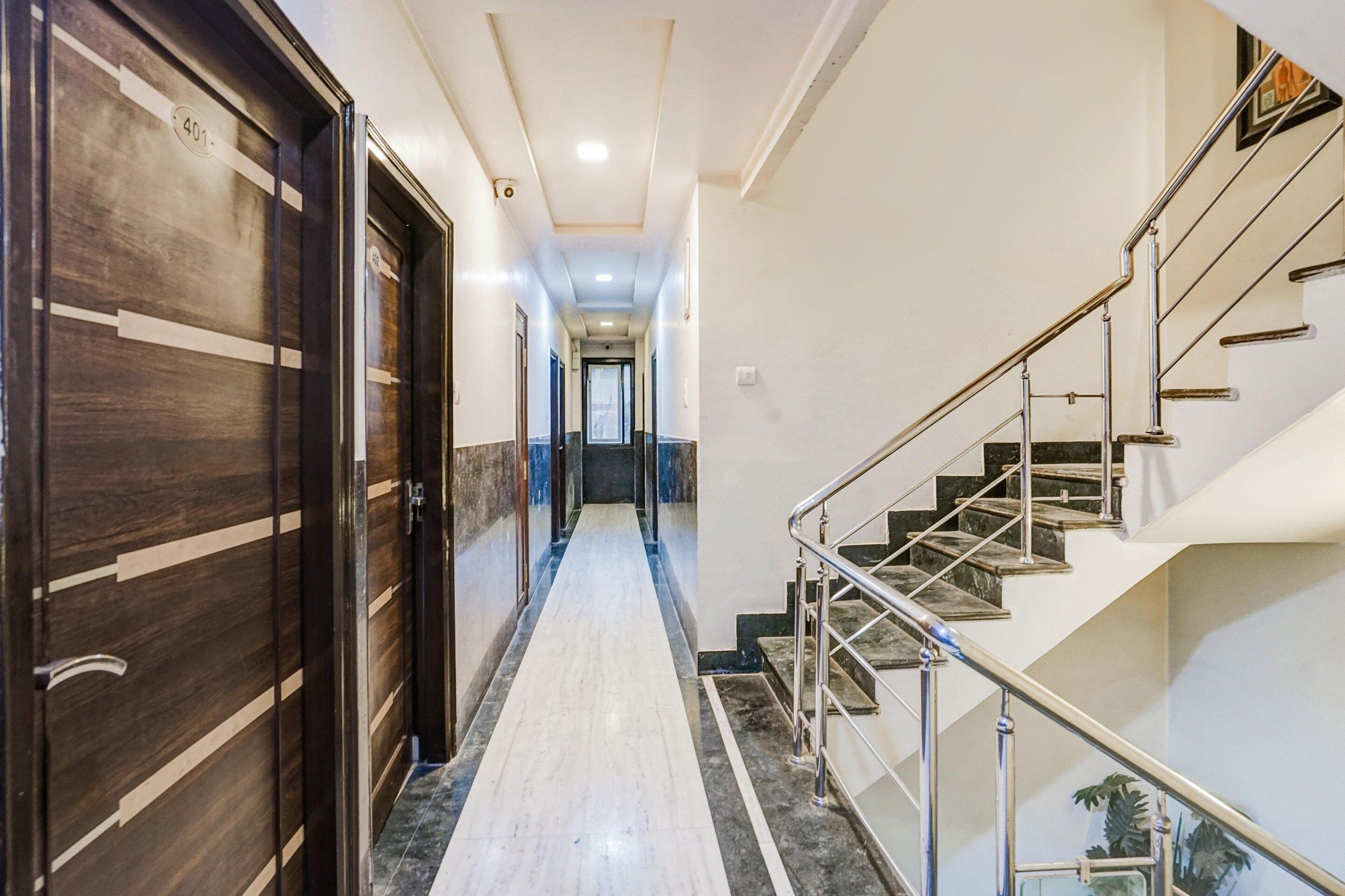 Corredor de hotel com piso de mármore, escada com grades de metal e portas de madeira com números.