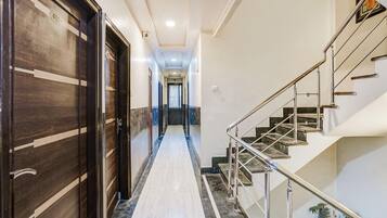 Corredor de hotel com piso de mármore, escada com grades de metal e portas de madeira com números.