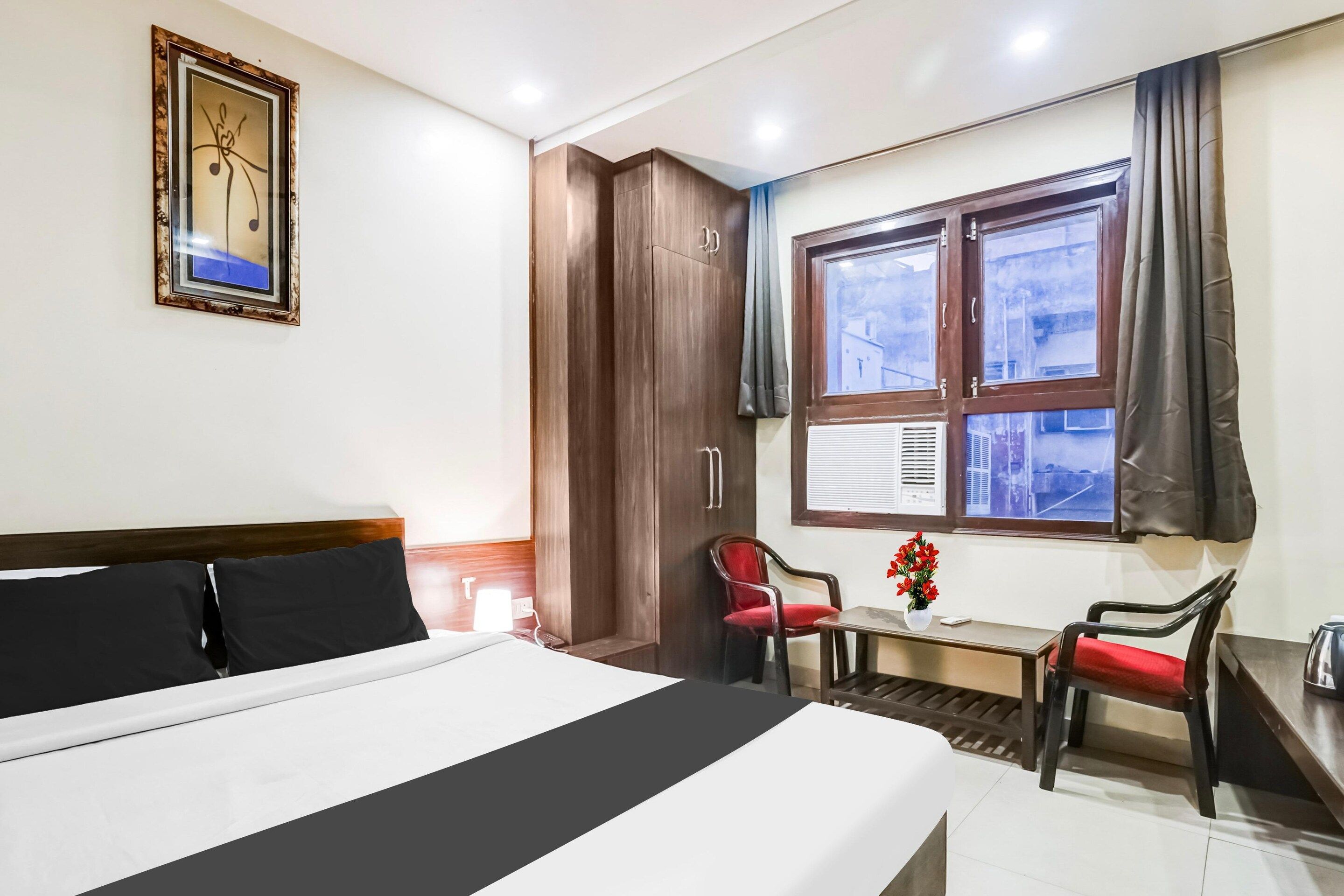 A hotel room with a bed, a desk, a chair, a window with curtains, and a framed picture on the wall.