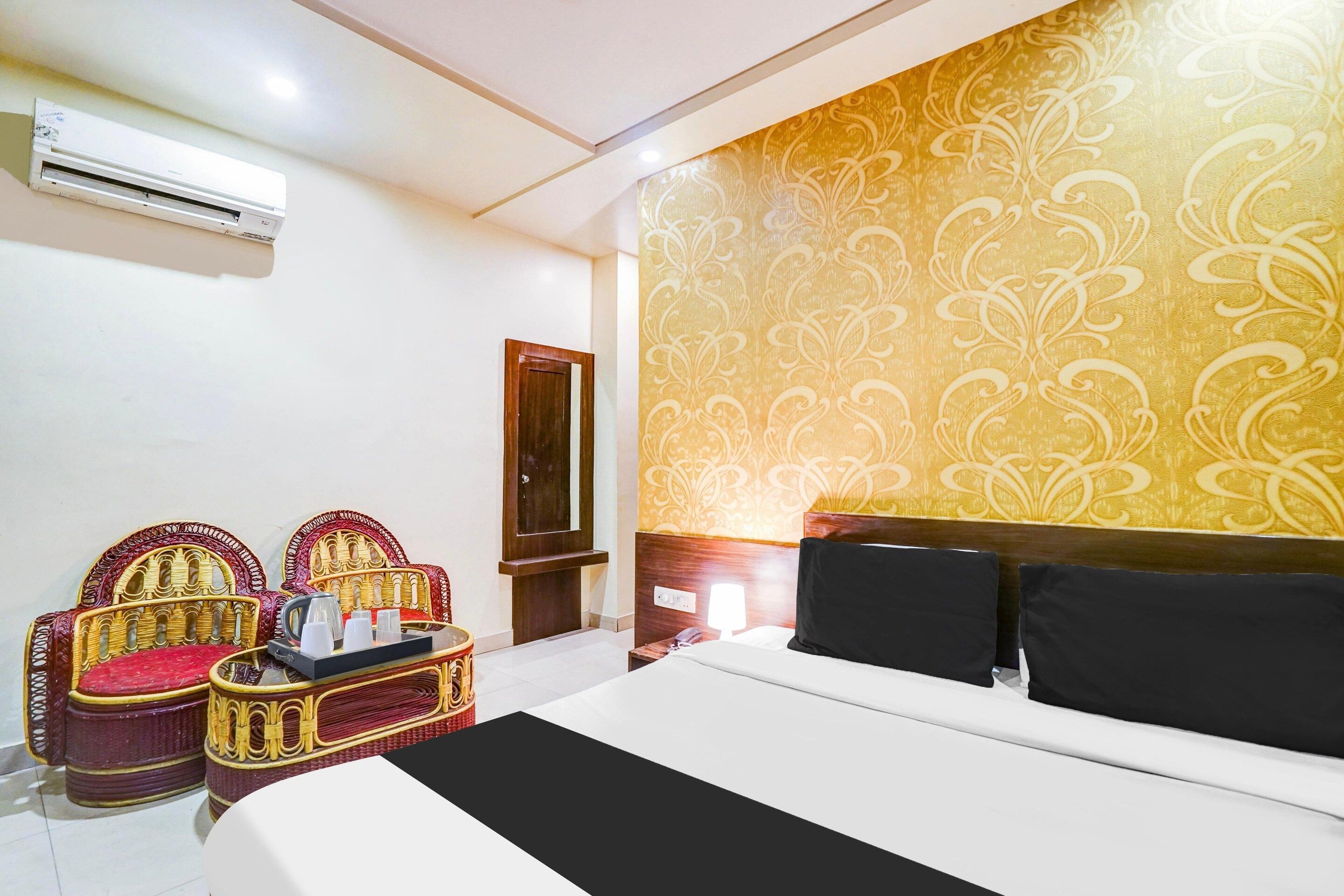 A hotel room with a bed, two chairs, a small table, and a wall-mounted air conditioner.