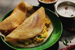 A plate with a folded crepe-like food item, possibly a crepe or pancake, filled with a yellow mixture, accompanied by a small bowl of white sauce and a red chili. - Super Collection O Sindhi Camp (Jaipur)