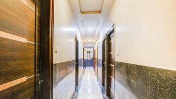 Corredor de hotel com portas de madeira à esquerda, piso de mármore e iluminação embutida no teto.