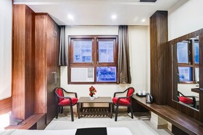 A hotel room with a large window, a wooden wardrobe, a small table with chairs, and a bedside table with a kettle. - Super Collection O Sindhi Camp (Jaipur)