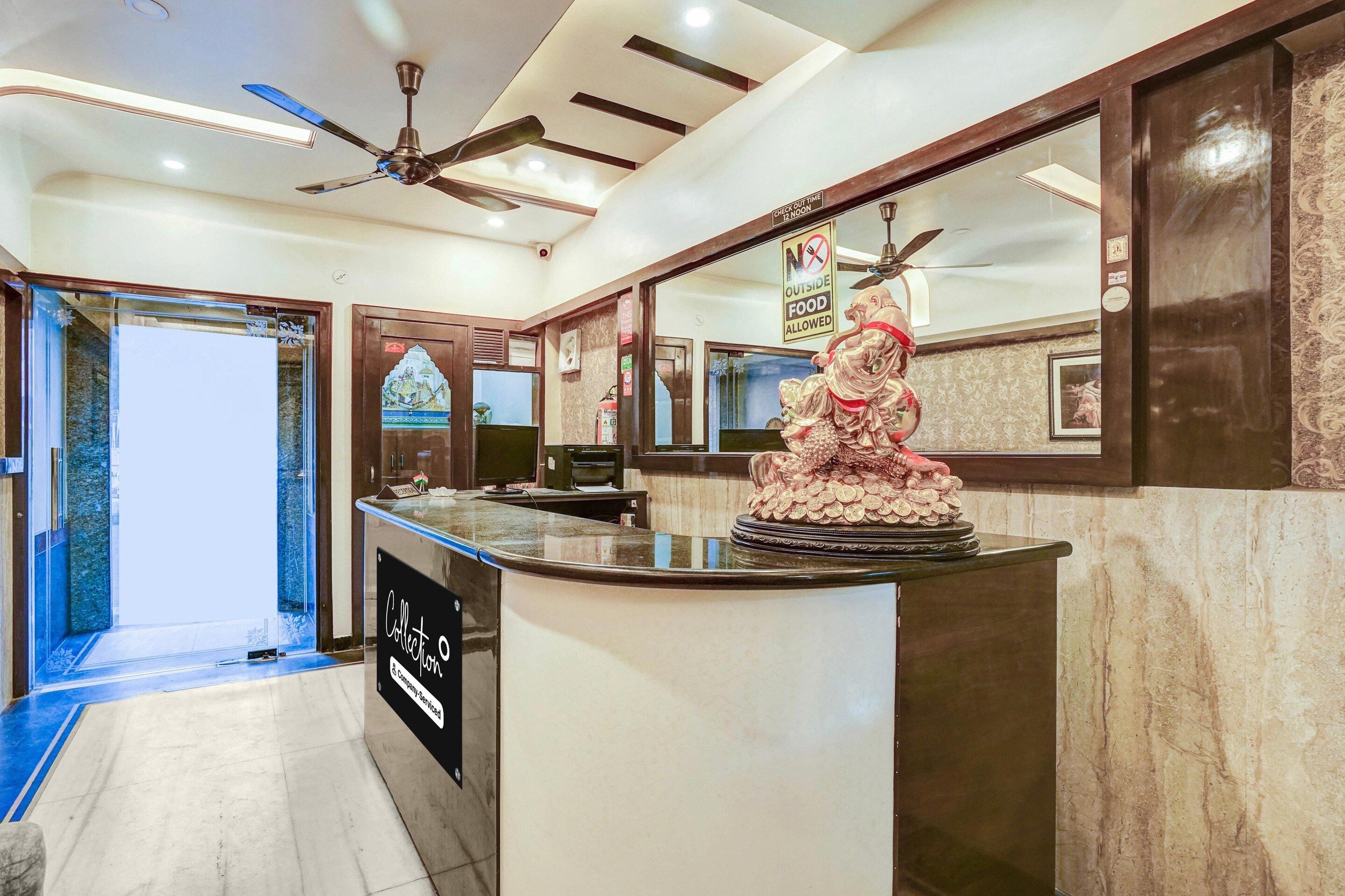 A reception area with a counter, a statue, a ceiling fan, and a sign indicating check-out time.
