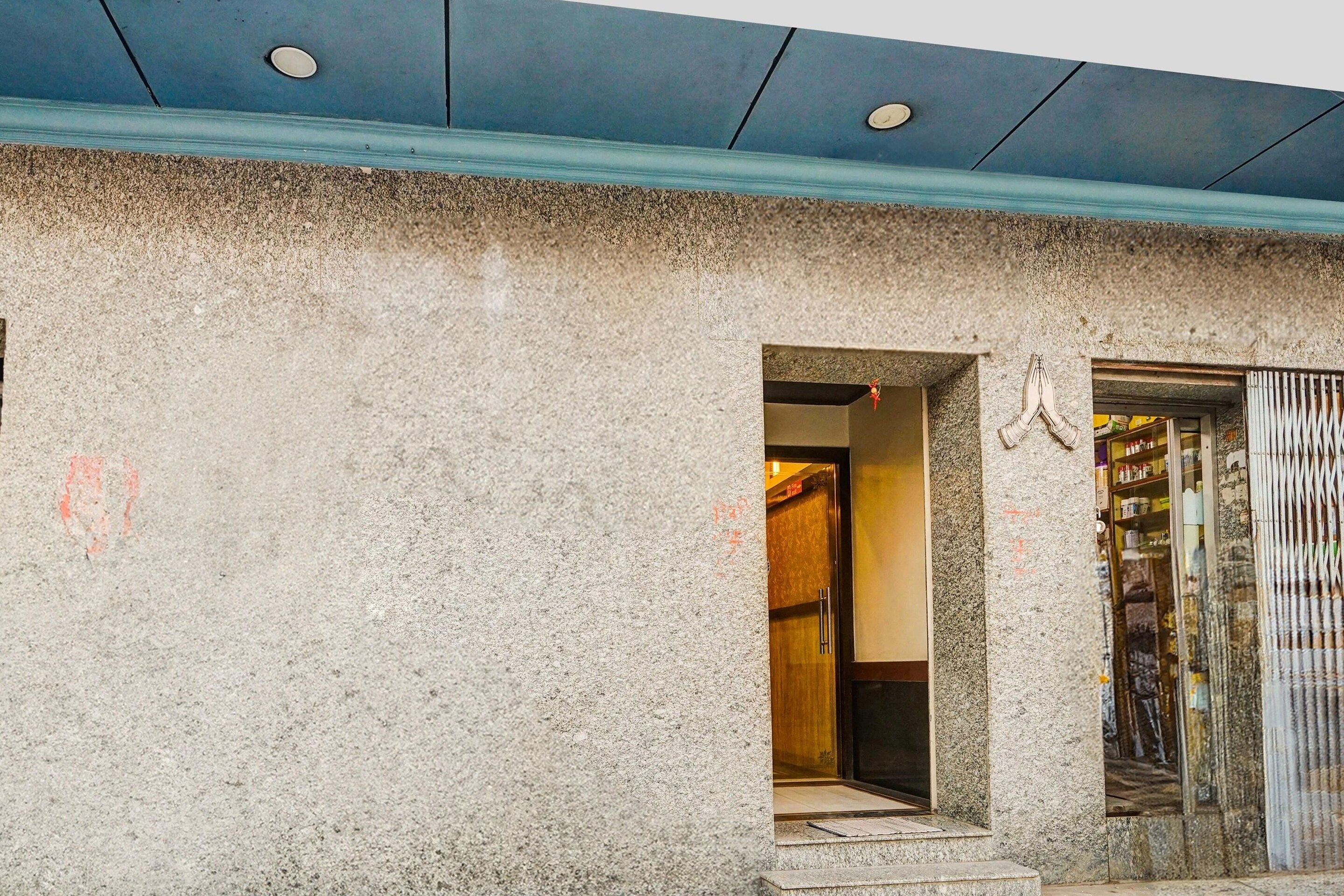 A building facade with a textured stone exterior, a doorway leading to an interior space, and a metal gate with a hand symbol.