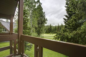 Blick vom Balkon mit Holzwertung auf einen Golfplatz, umgeben von dichtem Baumbestand.