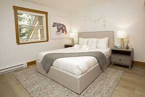 A bedroom with a bed, bedside tables, a window, a wall-mounted artwork, and a rug. - Alpine Greens 5 Star renovated townhouse (Whistler)
