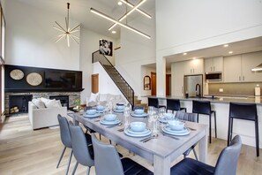 A modern kitchen with a central island, stainless steel appliances, and a dining area with a long table set for six. - Alpine Greens 5 Star renovated townhouse (Whistler)