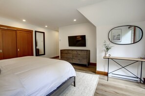 Ein Schlafzimmer mit einem großen Bett, einem Holzschrank, einem Schminktisch, einem Spiegel und einem an der Wand befestigten Flachbildfernseher.