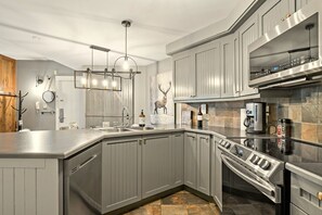 A modern kitchen with grey cabinetry, stainless steel appliances, and a central island. - Tremblant Prestige - Les Falaises 138-2 (Mont-Tremblant)