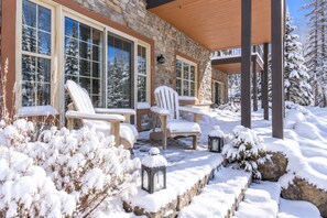 A stone building with large windows and a covered outdoor seating area with chairs and tables. - Tremblant Prestige - Les Falaises 138-2 (Mont-Tremblant)