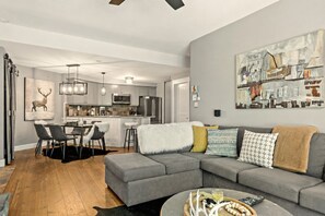 A modern living room with a gray sectional sofa, a dining area with a black rug, and a kitchen with stainless steel appliances. - Tremblant Prestige - Les Falaises 138-2 (Mont-Tremblant)