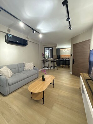 Un soggiorno moderno con un divano grigio, un tavolino in legno e una TV su un mobile.