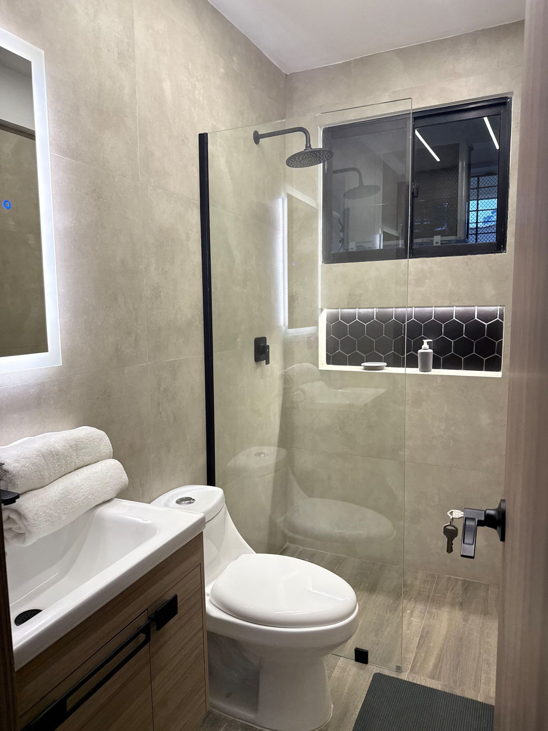 Une salle de bain moderne avec une douche à parois de verre, des toilettes blanches et un meuble-lavabo avec un miroir.