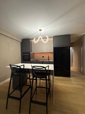 Una cucina moderna con un piano di lavoro in marmo, sedie nere e un lampadario originale.