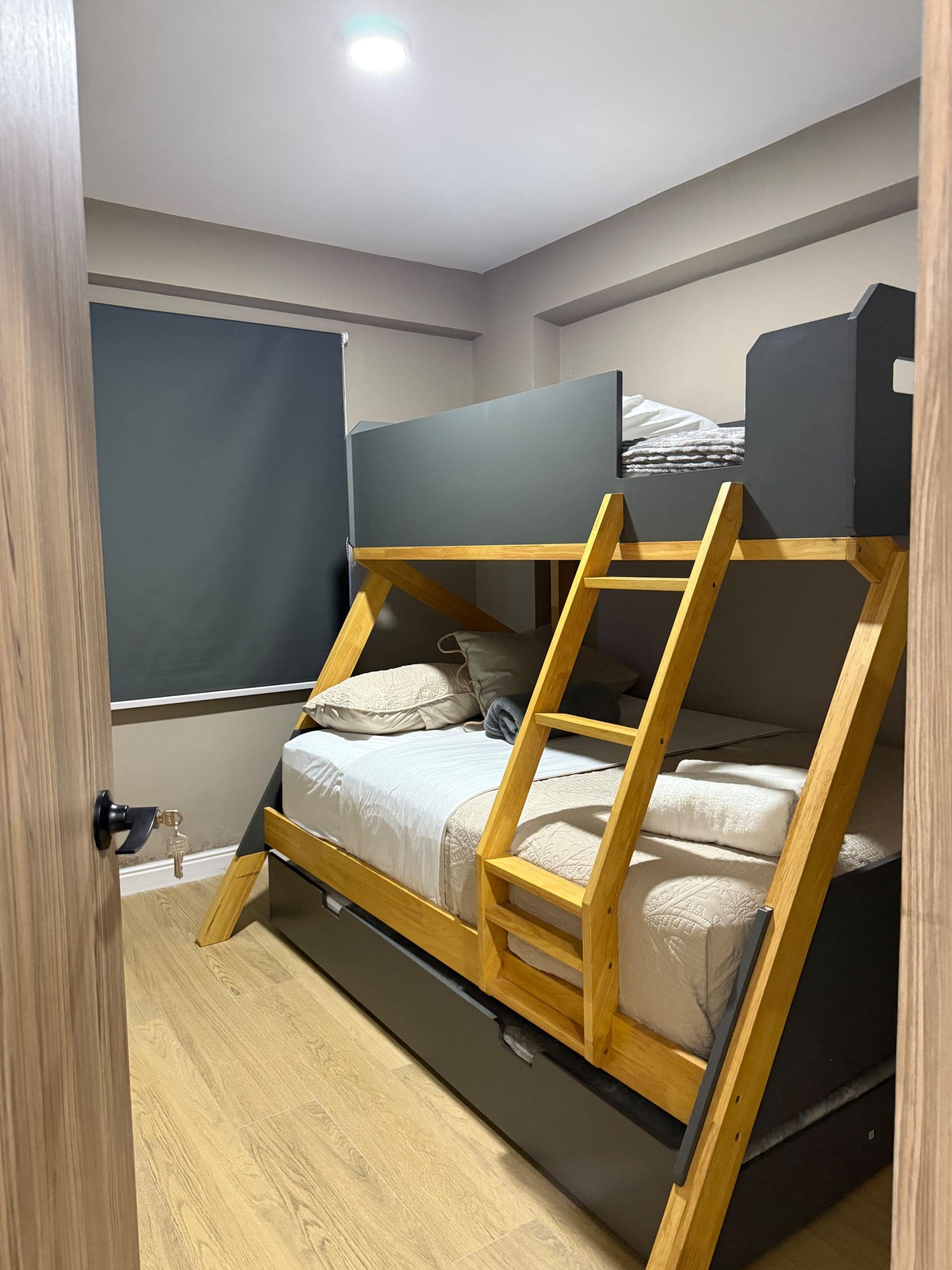 Een stapelbed met een houten trap, een raam met een zonnescherm en een deur met een sleutelslot.