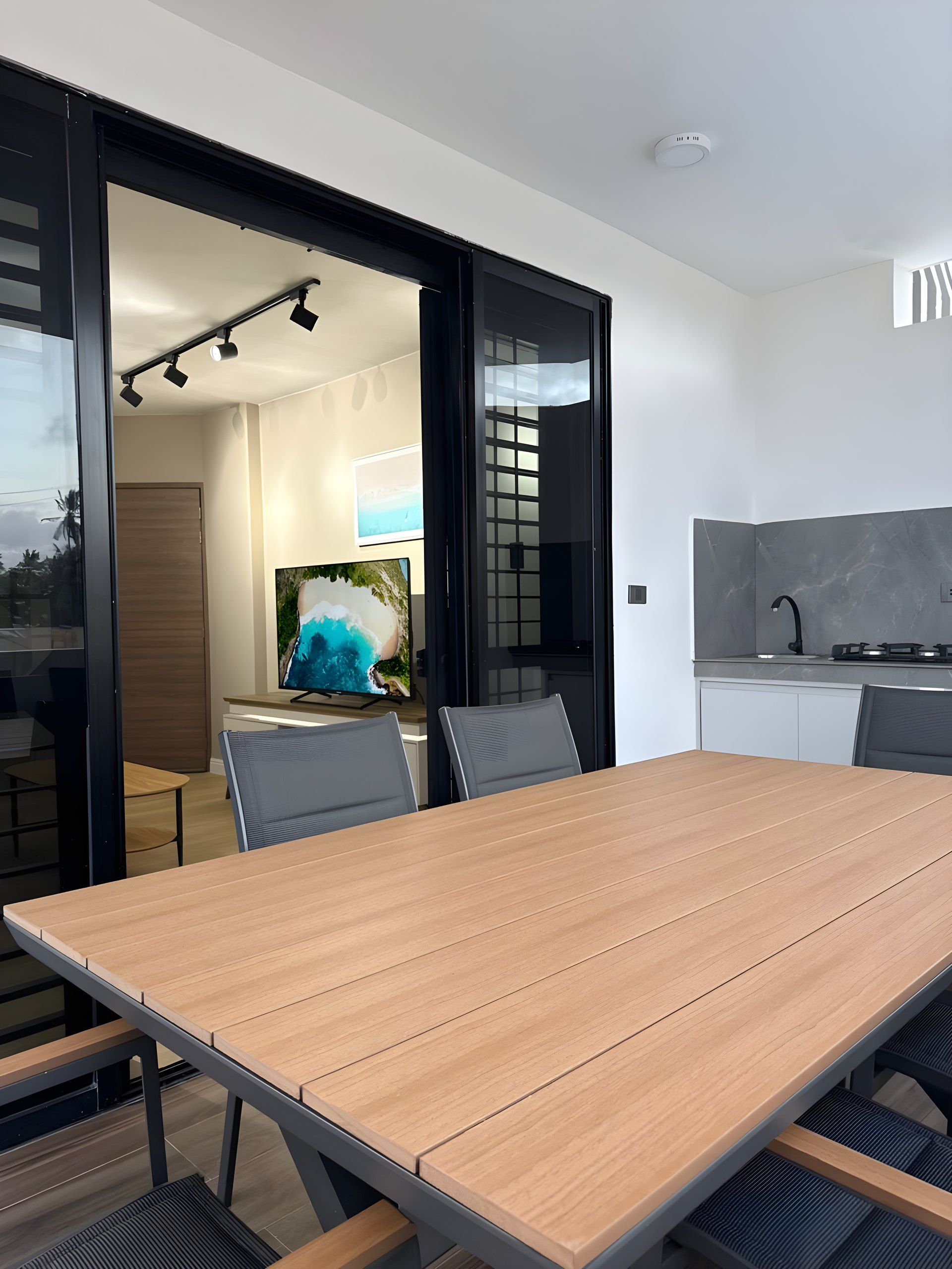 A modern dining area with a wooden table and chairs, a television, and a kitchen area with a stove.