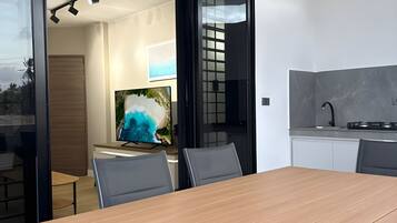 A modern dining area with a wooden table and chairs, a television, and a kitchen area with a stove.