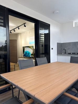A modern dining area with a wooden table and chairs, a television, and a kitchen area with a stove.
