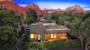 Una casa moderna amb un patí, envoltada d'arbres i formacions rocoses vermelles.