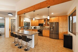 A modern kitchen with wooden cabinets, a large island with bar stools, stainless steel appliances, and pendant lighting. - NEW- Juniper Sky House: Rooftop Deck + Luxury (Sedona)