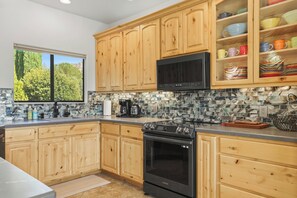 Une cuisine avec des meubles en bois, un four à micro-ondes, une cuisinière et une fenêtre donnant sur un paysage verdoyant.